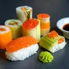 A close-up view of various sushi rolls and a small dish of soy sauce. Produktbild-Vorschau