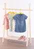 A children's clothing rack with several dresses and a pair of pink boots on the shelf below. Produktbild-Vorschau