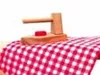 A wooden toy iron sits on a red and white checkered fabric, likely a tablecloth or ironing board cover. Produktbild-Vorschau