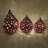 Three decorative lanterns shaped like teardrops, with star cutouts, are arranged in a row on a surface, casting light and shadows. Produktbild-Vorschau