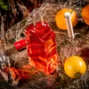 A bottle of red liquid with a lemon and oranges on a wooden surface with straw. Produktbild-Vorschau