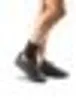 A close-up view of a person's legs and feet wearing black shoes. Produktbild-Vorschau