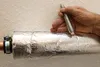 A hand is shown wrapping insulation around a copper pipe using wire from a spool. Produktbild-Vorschau