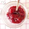 A close-up overhead view of jam in a glass jar with a spoon. Produktbild-Vorschau