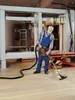 A man in a workshop is vacuuming sawdust from the floor. Podgląd zdjęcia produktu