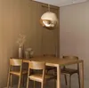 A dining room setting with a wooden table and chairs, illuminated by a unique pendant light. Produktbild-Vorschau
