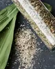 A close-up shot of spices in a glass container and spilled on a dark surface, with green leaves. Produktbild-Vorschau