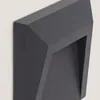 A close-up, angled view of a dark gray, geometric outdoor light fixture mounted on a light gray wall. Produktbild-Vorschau