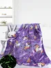 A purple blanket with unicorn and rainbow patterns is draped over a white bench, next to a white bunny pillow. A small circular inset shows a close-up of the blanket's glowing pattern. Náhled obrázku produktu