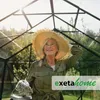 A woman in a straw hat is standing in a greenhouse, looking up at the sky. Produktbild-Vorschau