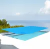A solar pool cover is placed on a swimming pool with a view of the ocean and trees in the background. Produktbild-Vorschau