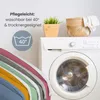 A washing machine with laundry and decorative items on top, with a stack of colorful textiles in the foreground. Produktbild-Vorschau