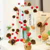 A string of Christmas lights with pinecones and red berries is draped over a stack of books. Produktbild-Vorschau