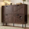 A dark wood cabinet with four doors, designed to look like barn doors, stands on black legs. It has a cutout on the right side, suggesting it's a cat litter box enclosure. A white ball hangs from a string inside one of the doors. Produktbild-Vorschau