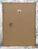 The back of a white distressed picture frame with a brown cardboard insert and hanging hardware. Produktbild-Vorschau