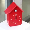 A red cuckoo clock shaped like a house sits on a white surface. Produktbild-Vorschau