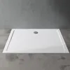 A white rectangular shower tray with a central drain is placed on a concrete floor in front of a grey concrete wall. Produktbild-Vorschau