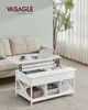 A white lift-top coffee table with storage is shown in a living room setting next to a beige sofa. A laptop, a cup of coffee, and blankets are on the table. Náhled obrázku produktu