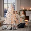A woman decorates a white Christmas tree in a cozy living room with gifts at its base. Náhľad obrázku produktu