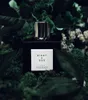 A perfume bottle and its packaging are displayed amongst lush green foliage and moss. Podgląd zdjęcia produktu