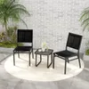 Two black chairs and a small table are set up on a patio with a brick wall and plants in the background. Produktbild-Vorschau