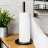 A black paper towel holder with a roll of white paper towels on a wooden countertop, next to a potted plant. The background is a white wooden wall. Náhľad obrázku produktu
