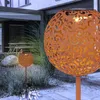 Two solar-powered garden lights with a decorative, perforated metal sphere in a rust color are shown in a garden setting at dusk. Produktbild-Vorschau
