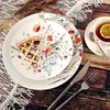 A slice of pie on a floral-patterned plate, with a cup of tea and cutlery on a wooden table. Anteprima dell’immagine prodotto