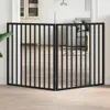 A black metal pet gate with two folding panels is shown in a doorway, with a living room visible in the background. Produktbild-Vorschau