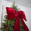 A close-up of a Christmas tree decorated with a large red velvet bow and a red ornament. Náhľad obrázku produktu