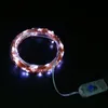 A coiled string of white LED lights with a copper wire, connected to a small battery pack with a blue button, on a black background. Produktbild-Vorschau