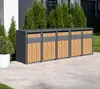 A row of five outdoor trash bins with wood-look doors and gray frames, set on a paved patio with greenery in the background. Náhled obrázku produktu