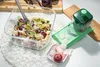 A salad in a glass bowl next to a green vegetable slicer and sliced radishes. Produktbild-Vorschau