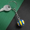 A key chain with a volleyball charm and a key, placed on a split green and black background. Produktbild-Vorschau