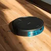 A black robot vacuum cleaner with a blue water tank sits on a wooden floor, illuminated by sunlight streaming from the side. Náhled obrázku produktu