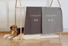 A dog is lying on a fluffy rug next to a wooden structure holding two blankets. The blankets have text and icons on them. Produktbild-Vorschau
