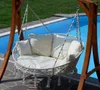 A white hanging chair with cushions is suspended from a wooden frame next to a swimming pool. Produktbild-Vorschau