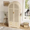 A wardrobe with woven doors and drawers, placed in a room with a stool, vase, and a window view. Podgląd zdjęcia produktu