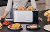 A person is standing behind a toaster with bagels in it, with various breakfast items on the counter. Voir les images du produit