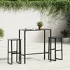 A black bar table and two stools are set up on a patio with a white wall and greenery in the background. Produktbild-Vorschau