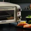 A vintage-style toaster oven is shown on a countertop with prepared food items. Náhled obrázku produktu