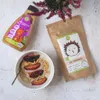 A flat lay of breakfast items including a bowl of oatmeal with plums and peanut butter, a bottle of peanut butter, and a bag of oat flakes, with a sprig of heather in the background. Podgląd zdjęcia produktu
