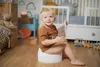 A young child sits on a potty in a nursery, reading a book. Produktbild-Vorschau