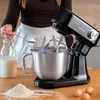 A person is adding flour to a stand mixer while preparing to bake. Produktbild-Vorschau