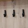 Three black coat hooks are mounted on a wooden panel. Produktbild-Vorschau