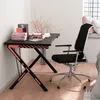 A gaming desk and chair set up in a room with a window and a bed. Produktbild-Vorschau
