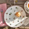 A close-up overhead view of a Villeroy & Boch Petite Fleur breakfast plate with a cream puff and a fork with a flower on a wooden table. Podgląd zdjęcia produktu
