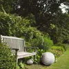 A garden bench sits in a lush garden with two decorative stone spheres in front of it. Anteprima dell’immagine prodotto