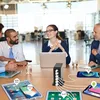 People in a meeting room, with a charging station and multiple devices on a table. Produktbild-Vorschau