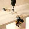 A drill with a depth stop is drilling a hole in a wooden board, with wood shavings scattered around. Corner clamps are used to hold the wood in place. Produktbild-Vorschau